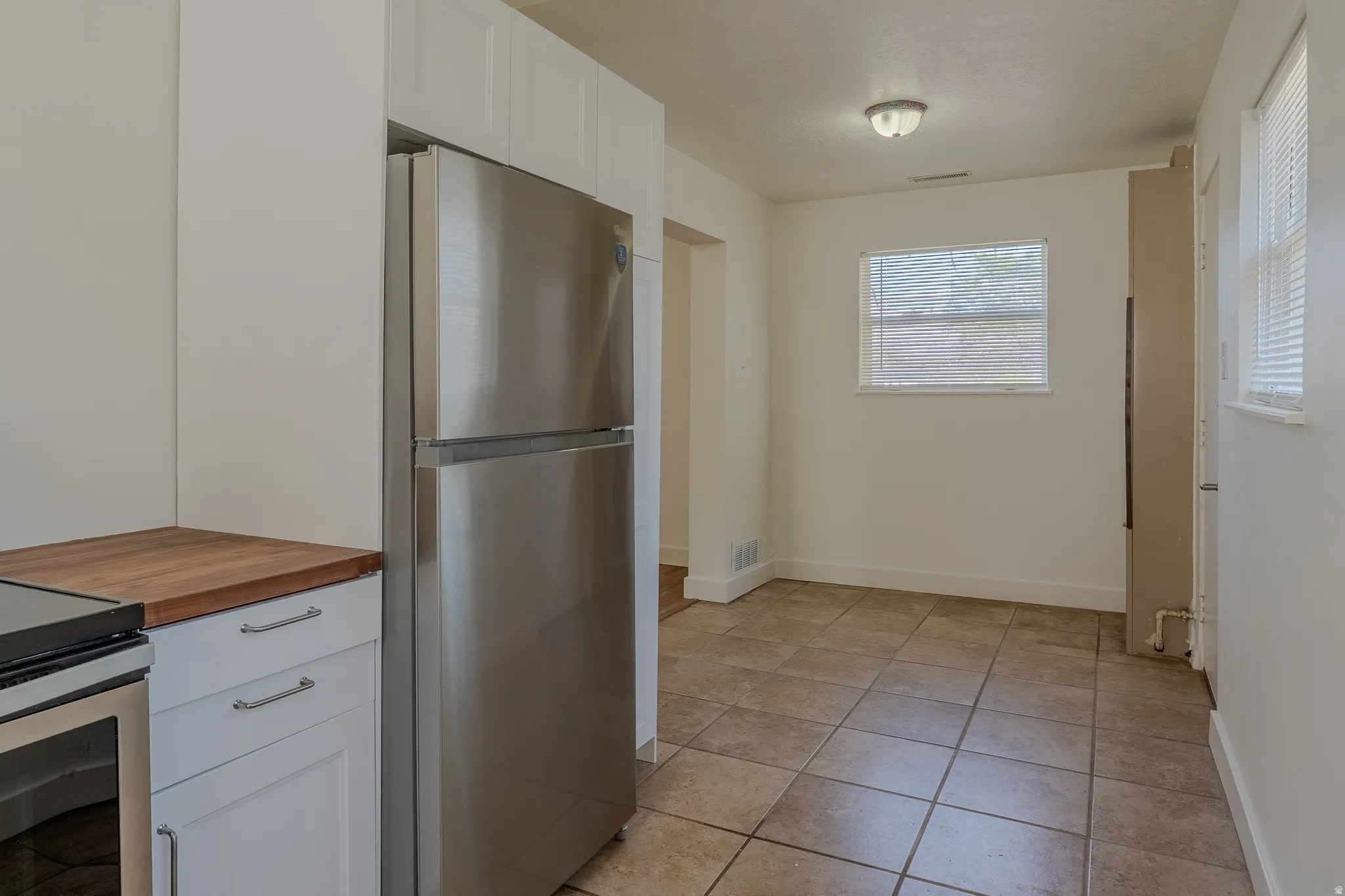 Kitchen space featuring a stainless steel refrigerator, white cabinetry with silver hardware, butcher block countertops, and tile flooring