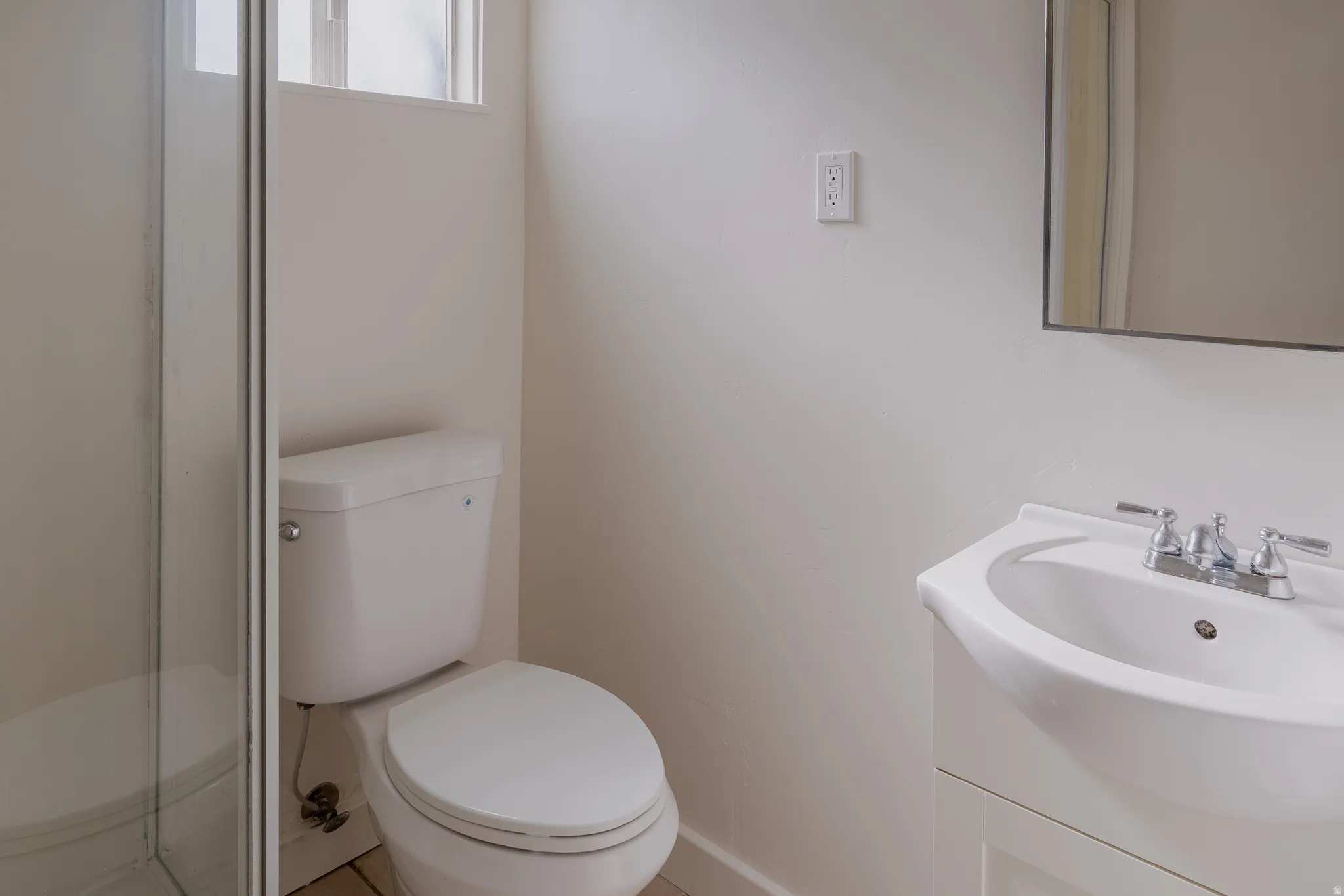 Bathroom featuring a white toilet, glass shower enclosure, and a vanity with an integrated sink and chrome faucet