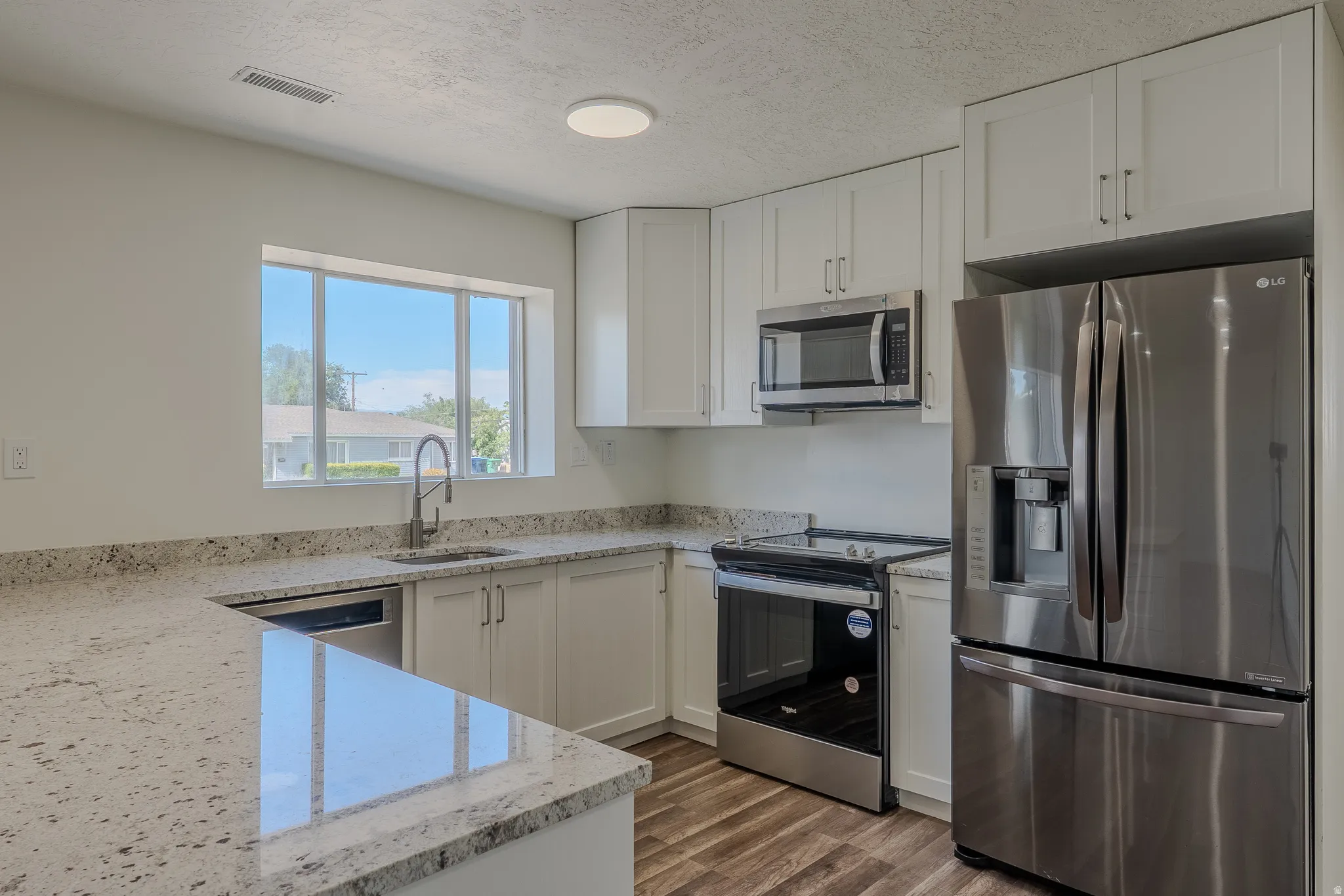 Kitchen featuring white cabinetry, light-toned countertops, stainless steel appliances, and wood-finish flooring