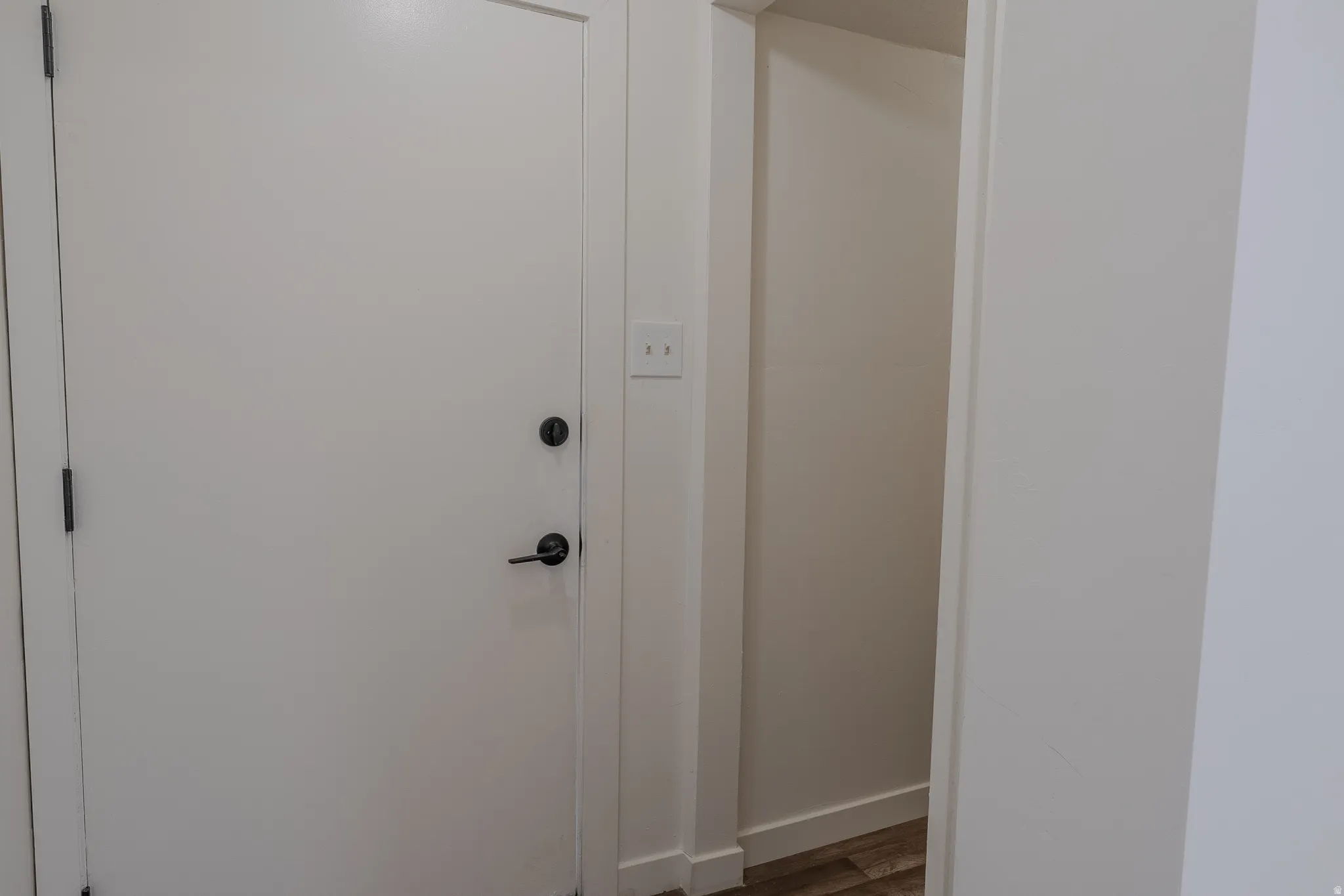 White interior door with contemporary black hardware, light switch panel, and an open storage niche with wood-finish flooring