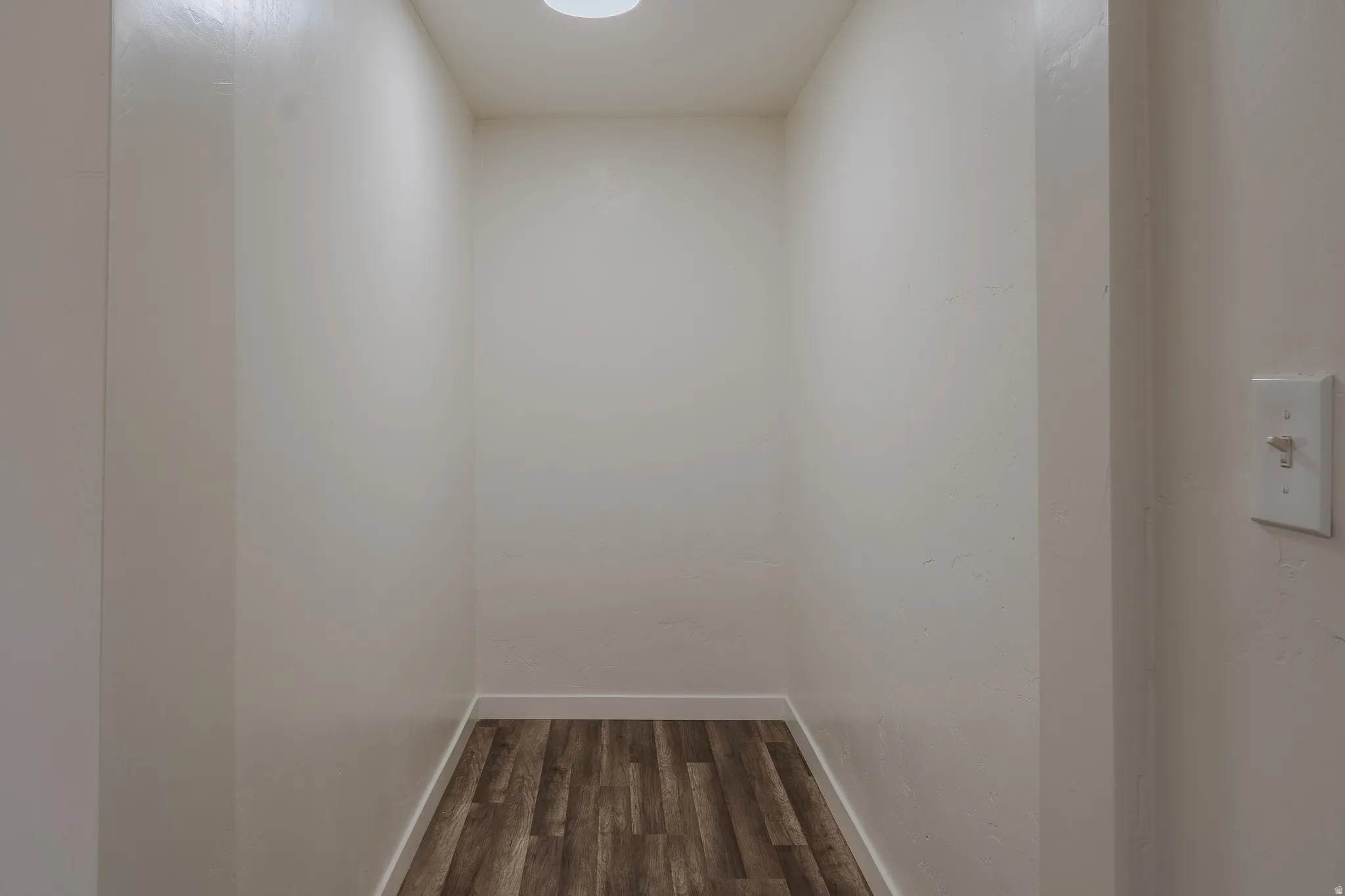 Recessed storage nook featuring wood-finish flooring, white baseboards, and a ceiling-mounted light fixture