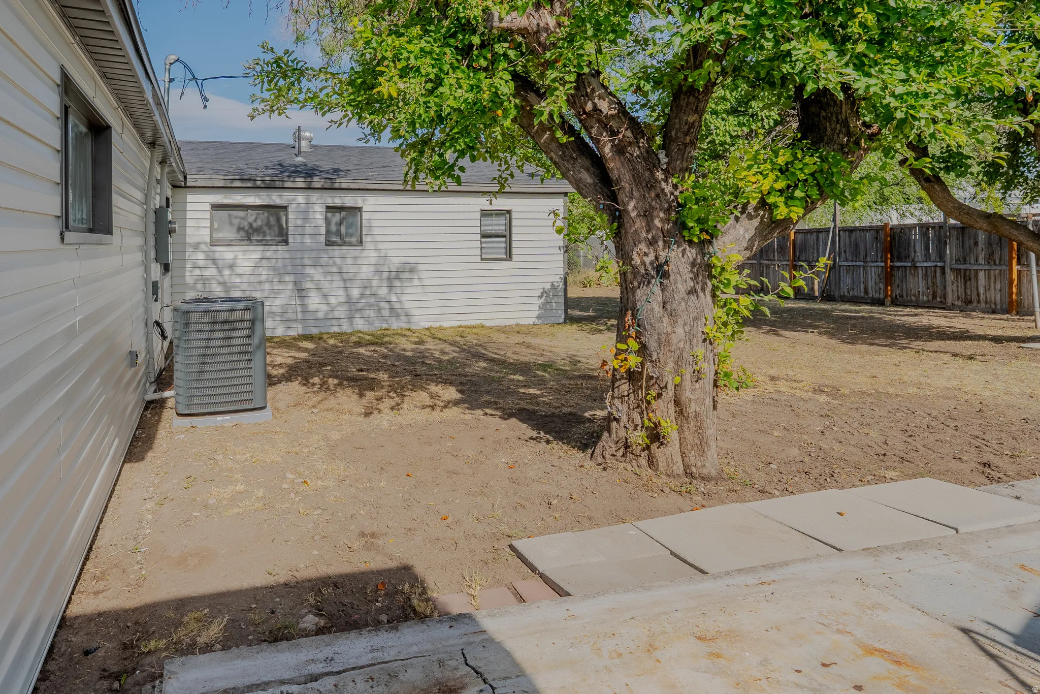 Rear yard area featuring a mature shade tree, a wood privacy fence, and a white siding exterior