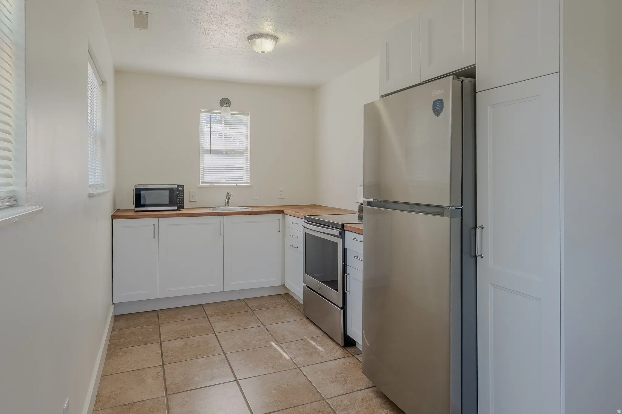 Kitchen featuring white shaker-style cabinetry, wood-finish countertops, and stainless steel appliances
