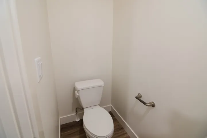 Compact powder room with wood-finish flooring, a white toilet, and a brushed nickel toilet paper holder