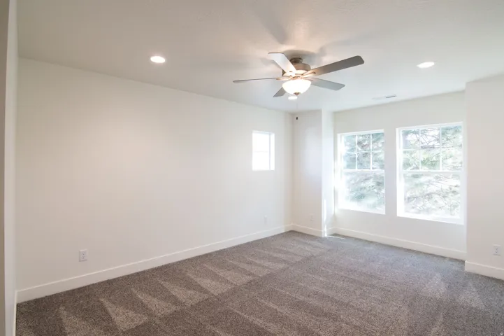 Room featuring light gray patterned carpeting, recessed lighting, a ceiling fan with integrated lighting, and three windows offering natural illumination