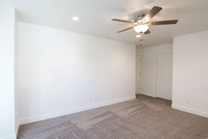 Spacious interior room featuring a ceiling fan with integrated lighting, recessed ceiling lights, white baseboards, and neutral-toned carpeting