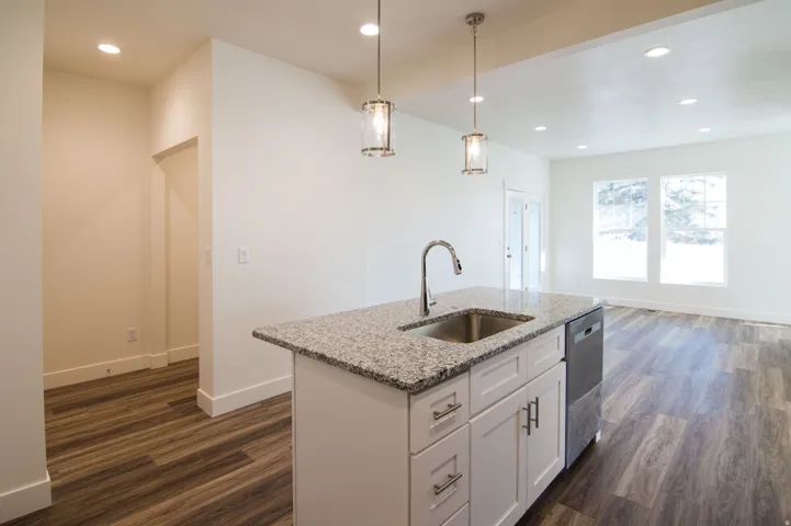 Kitchen island featuring a stainless steel sink, gooseneck faucet, light granite countertop, and white cabinetry with brushed nickel hardware