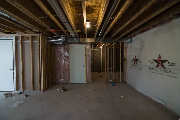 Unfinished basement featuring exposed wood joists and subflooring, framed interior walls, visible ductwork, and two white paneled doors
