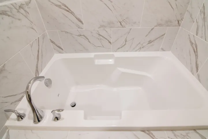 Built-in soaking tub with chrome fixtures, surrounded by large format marble-look tile
