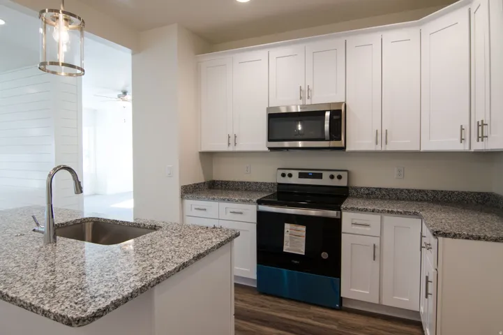 Contemporary kitchen featuring white shaker cabinetry, speckled countertops, stainless steel appliances including a built-in microwave and range, and wood-finish flooring