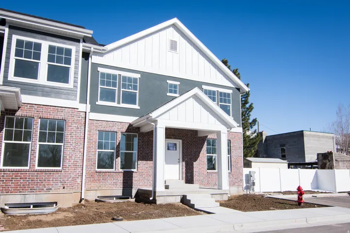 New construction featuring a brick and siding exterior, a prominent front entrance with a covered porch, multiple windows with grid patterns, and a paved sidewalk