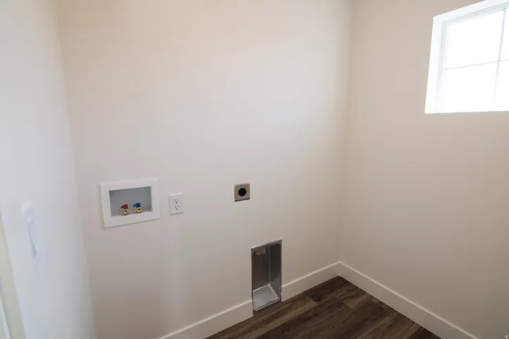 Dedicated laundry space featuring a high window, wood-finish flooring, white baseboards, and essential utility hookups