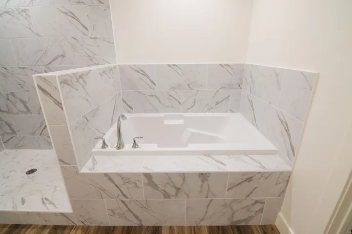 Built-in soaking tub with chrome fixtures, surrounded by large format marble-look tile