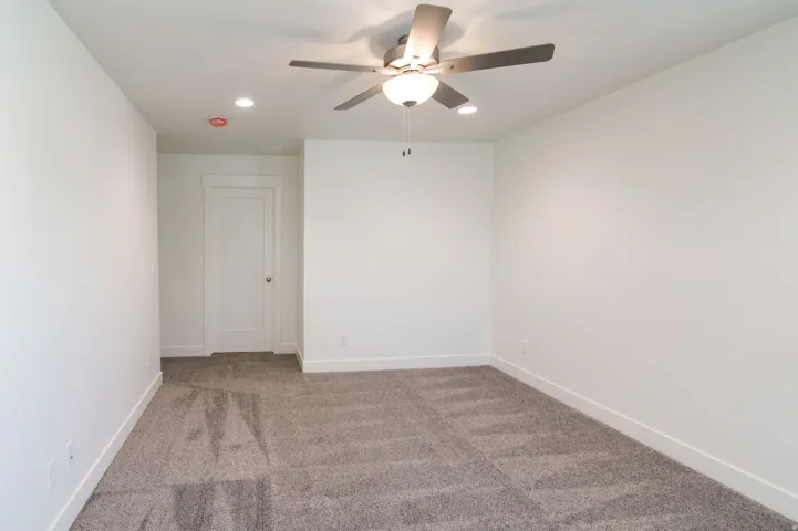 Spacious room featuring neutral carpeting, white walls, and a modern ceiling fan with integrated lighting