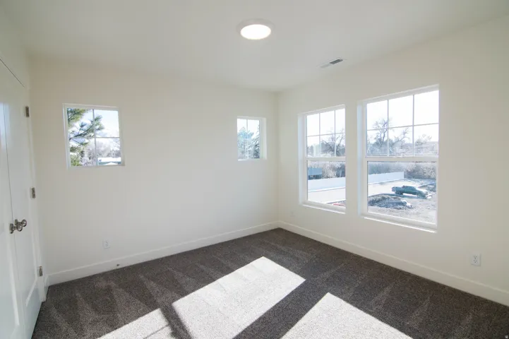 Bright interior space featuring white walls, gray carpet flooring, multiple windows, and a recessed ceiling light fixture