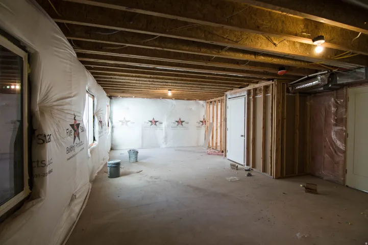 Unfinished basement space featuring exposed wood joists, concrete flooring, multiple windows, framed wall sections, and a solid white door