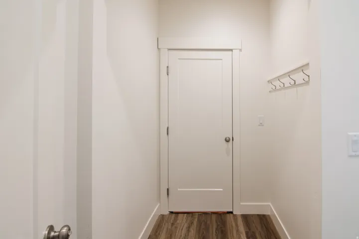 Entryway featuring a solid core door with brushed nickel hardware, wood-finish flooring, white baseboards, and a wall-mounted coat rack