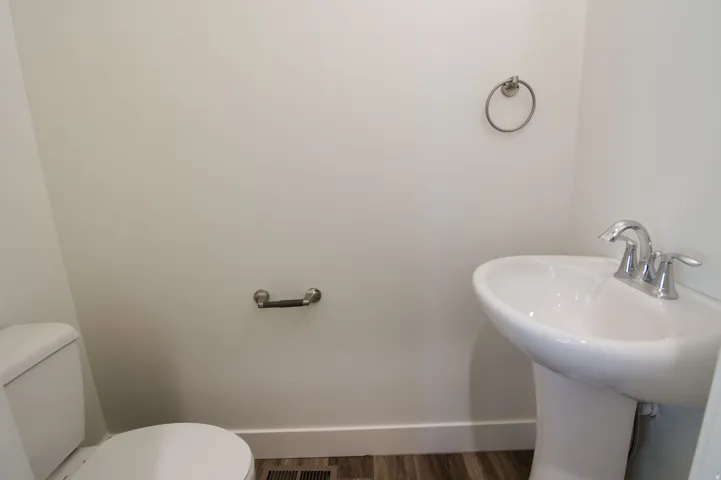 Pedestal sink with chrome faucet, white toilet, and wood-finish flooring