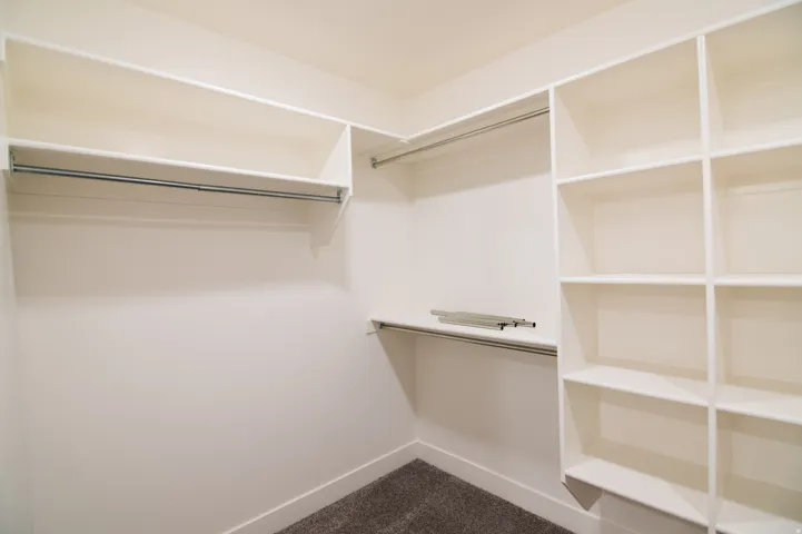 Organized closet space featuring white shelving, multiple hanging rods, and dark gray carpeting