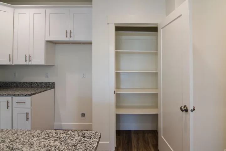 Kitchen pantry with five built-in shelves, white shaker cabinetry, speckled countertops, and wood-finish flooring