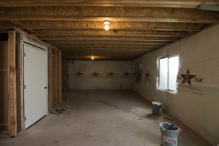 Unfinished basement featuring exposed wood joists and subflooring, framed interior walls, multiple windows, and a solid core door