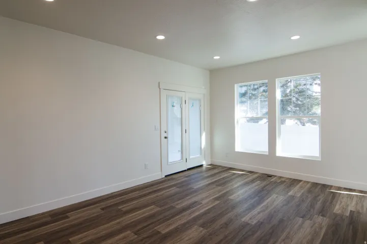 Spacious room featuring wood-finish flooring, recessed ceiling lighting, a glass-paned door, and two large windows with exterior tree scenery