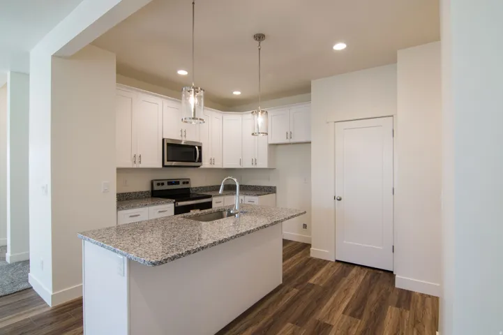Open-concept kitchen featuring white cabinetry, stainless steel appliances, granite countertops, a kitchen island with an integrated sink, and wood-finish flooring