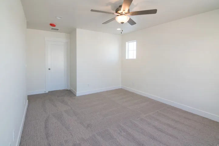 Carpeted interior space featuring a ceiling fan with integrated lighting, a white panel door, and a single window with grid panes