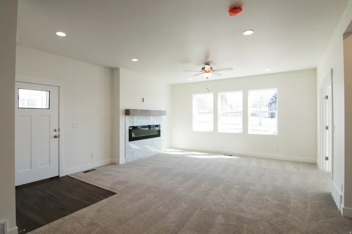 Spacious living area featuring a linear electric fireplace with a wood-finish mantel and tile surround, three large windows, a ceiling fan, and recessed lighting