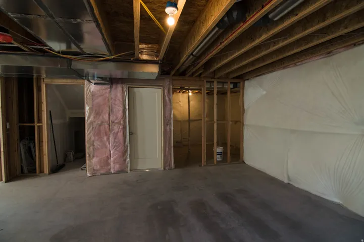 Unfinished basement featuring exposed wood joists, concrete flooring, and partial framing for future customization