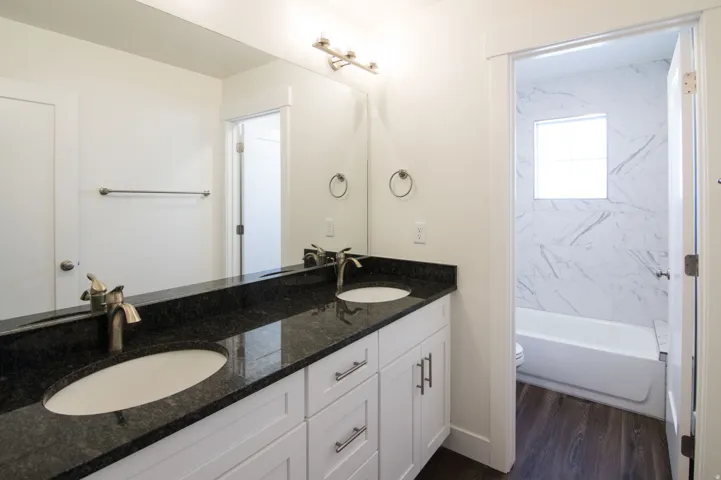 Dual vanity with dark stone countertop, white shaker cabinetry, and brushed nickel hardware