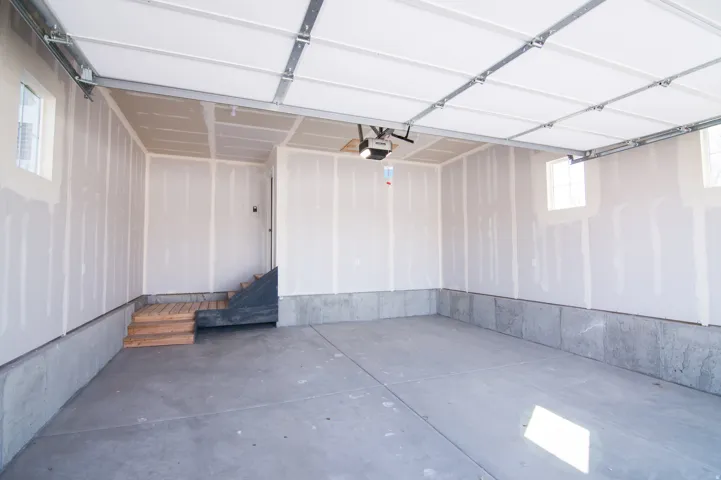 Spacious garage featuring a concrete floor, three windows, and an interior access door with wooden steps
