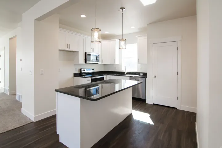 Kitchen featuring white cabinetry, dark countertops, a central island, stainless steel appliances, and dark wood-finish flooring