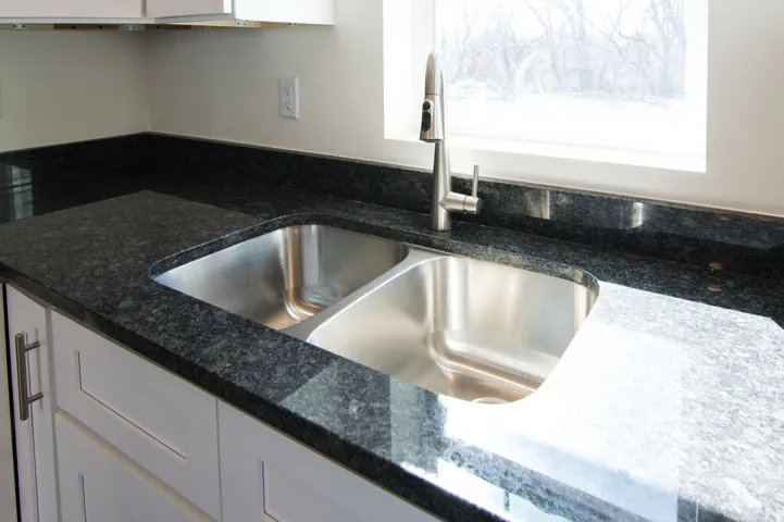 Stainless steel double basin sink with a single-handle pull-down faucet set against dark stone countertops
