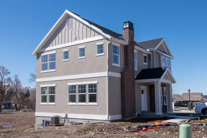Two-story residence featuring a stucco exterior with broad white trim, a gabled roofline, and a prominent brick chimney