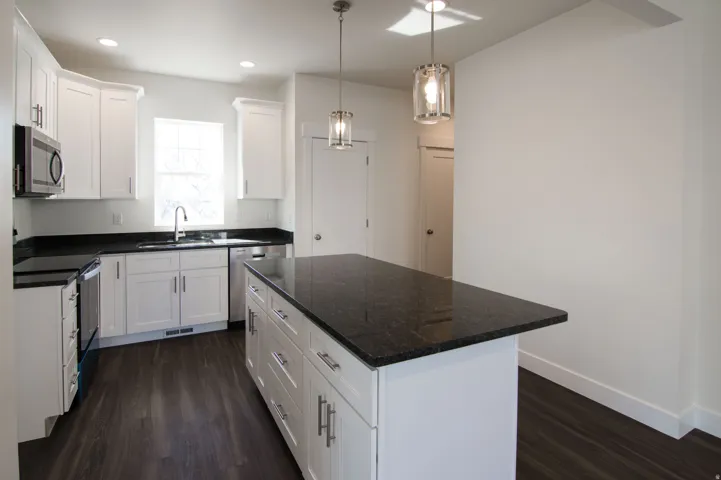 Kitchen featuring a central island with dark stone countertops, white cabinetry, stainless steel appliances, wood-finish flooring, and recessed lighting