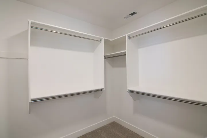 Walk-in closet featuring built-in white shelving, multiple hanging rods, and neutral-toned carpet flooring