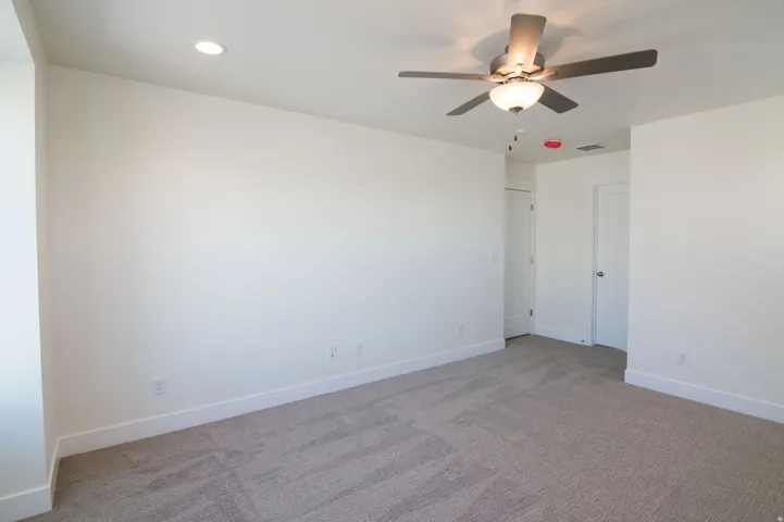 Spacious room featuring neutral carpet, white walls, recessed lighting, and a ceiling fan with light fixture