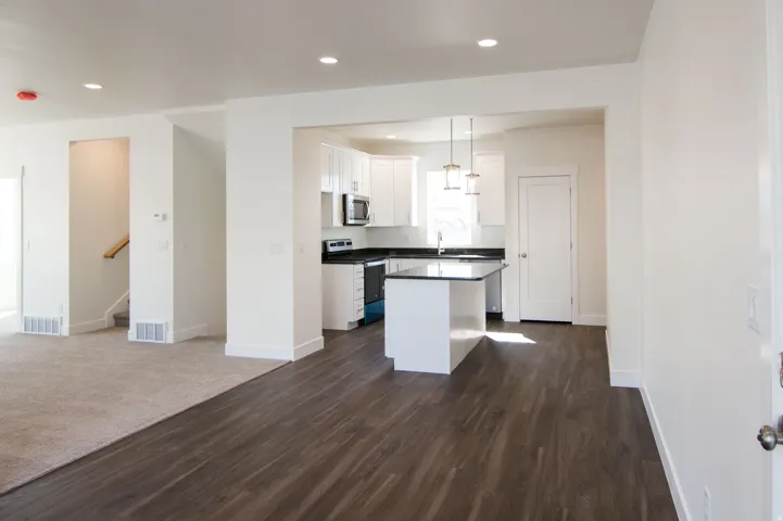 Open-concept living area featuring dark wood-finish flooring, recessed lighting, and a white kitchen with a center island