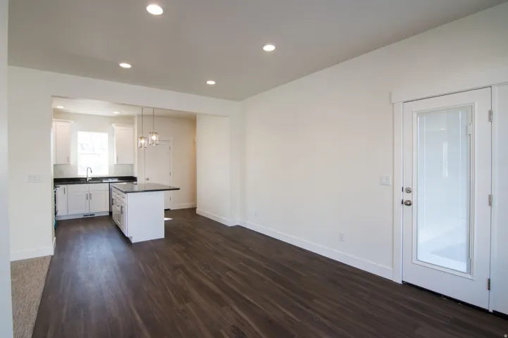 Open-concept living space with dark wood-finish flooring, recessed lighting, and a white interior door with a full-lite glass panel