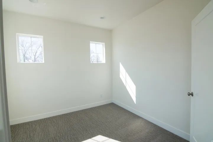 Bright room featuring two windows, recessed ceiling lighting, a textured gray carpet, and white baseboards