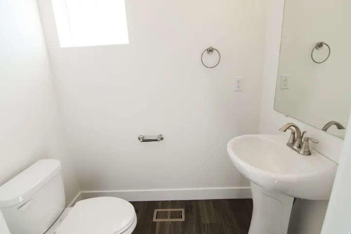 Powder room featuring a pedestal sink with a brushed nickel faucet, a white toilet, and wood-finish flooring