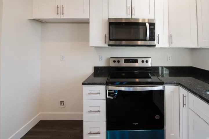 Kitchen featuring white cabinetry, dark stone countertops, stainless steel appliances including a range and microwave, and dark wood-finish flooring
