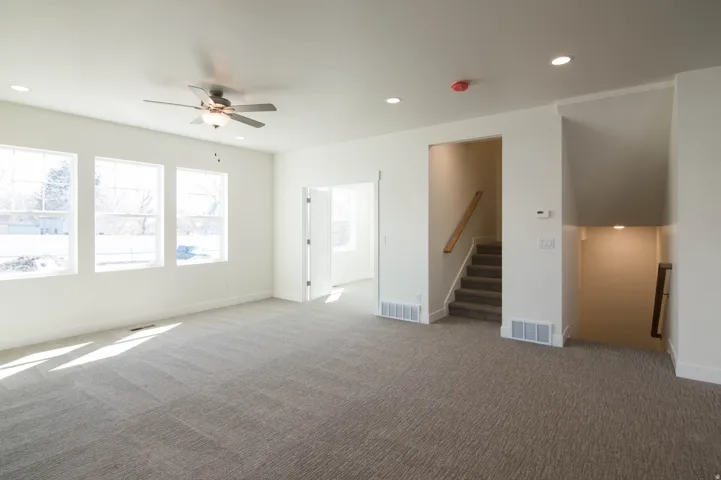 Spacious living area featuring neutral-toned carpet, multiple windows, and a ceiling fan with integrated lighting
