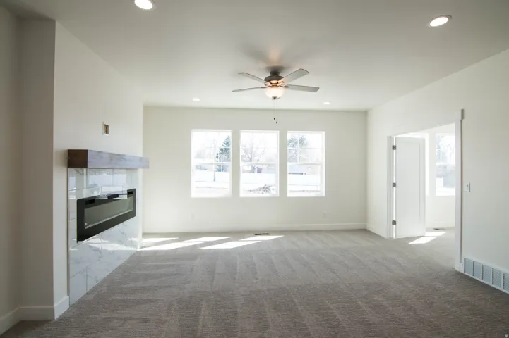 Spacious room featuring a contemporary fireplace with a wood-finish mantel and tile surround, triple windows, recessed lighting, and a ceiling fan