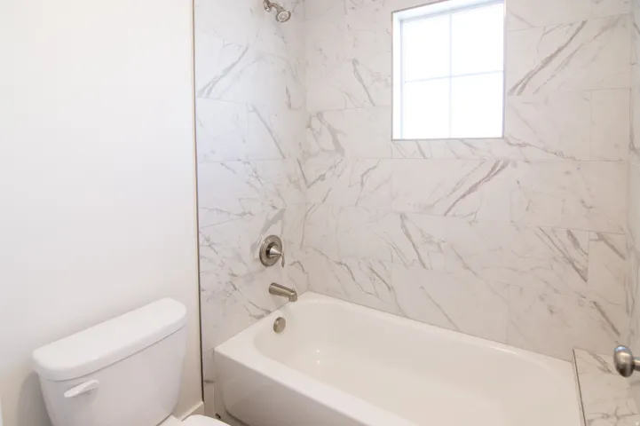 Bathtub and shower combination featuring large format marble-look tile surround, brushed nickel fixtures, and a transom window