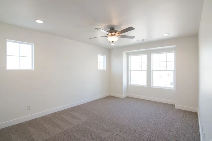 Spacious room featuring neutral carpeting, recessed lighting, a ceiling fan, and multiple windows with white trim