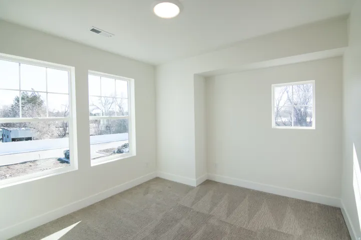 Bright room featuring three windows, neutral wall paint, white trim, and patterned carpet flooring