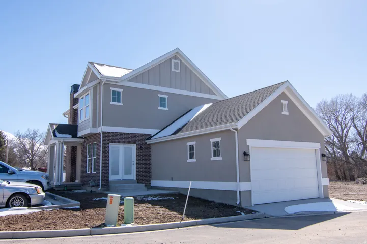 Contemporary architecture featuring a two-car garage, stucco siding, brick detailing, and a prominent front entrance with double doors and a covered porch