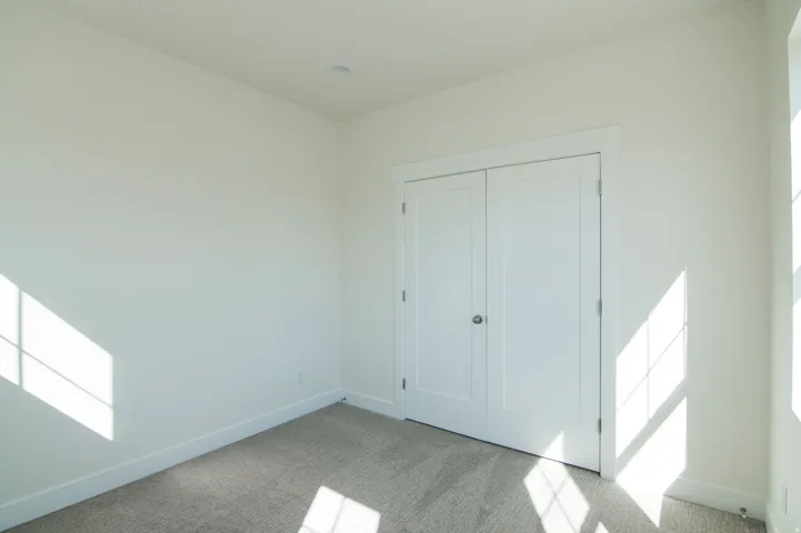 Neutral-toned carpeted room featuring white walls and a double-door closet with chrome hardware